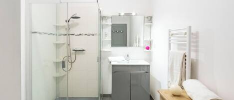 A modern bathroom with a glass shower enclosure, a sink with a mirror, and a wooden bench.