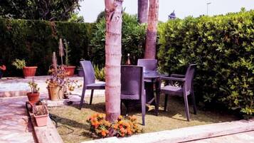 Area patio esterna con tavolo e sedie, circondata da piante in vaso e un piccolo bouquet di fiori.