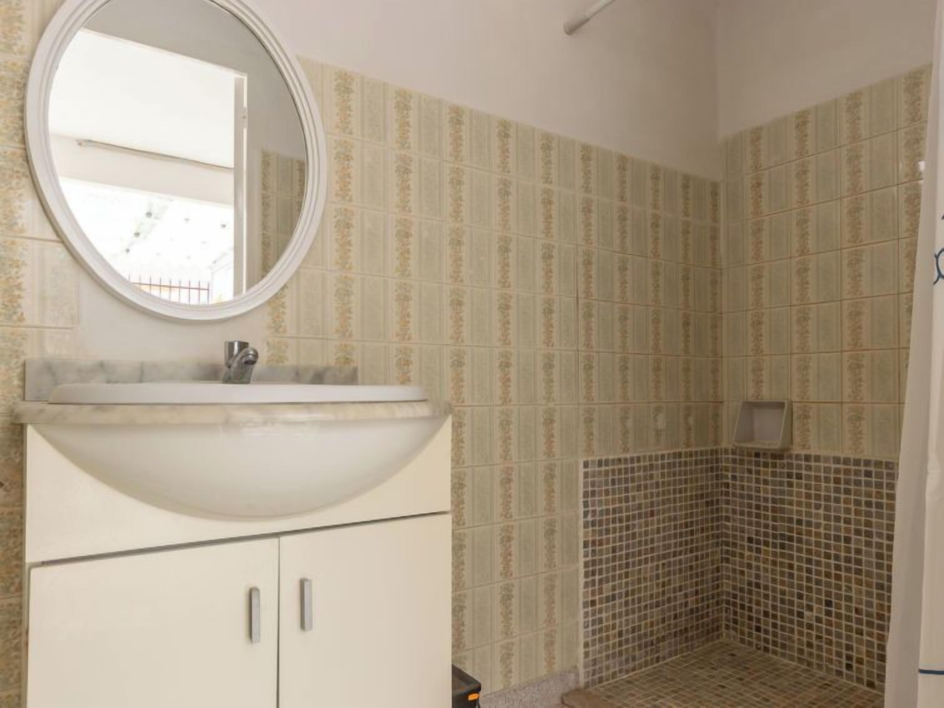 A bathroom with a sink, mirror, and tiled shower area.