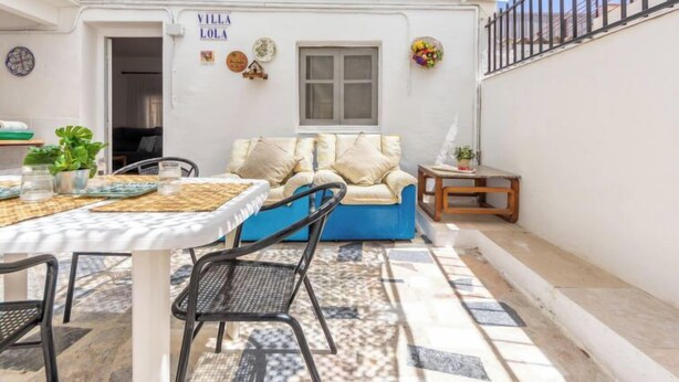 En mysig uteplats med en blå soffa, ett litet bord och en stol. På väggen finns en skylt med texten ”VILLA LOLA”.