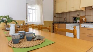 En matplats med ett träbord, stolar och ett fönster med gardiner. Det finns också ett köksområde med skåp och en spis.
