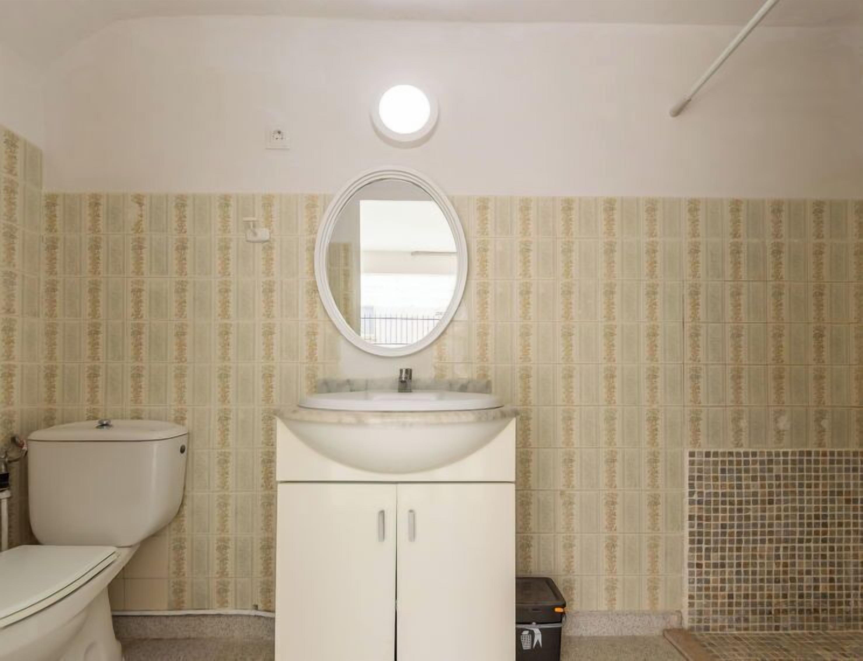 A bathroom with a toilet, a sink with a mirror, and patterned wallpaper.