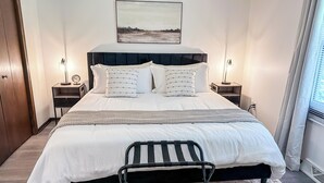 A neatly arranged bedroom with a bed, bedside tables, a chair, and a painting on the wall.