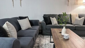 A modern living room with two grey sofas, striped pillows, a wooden coffee table, and a plant.