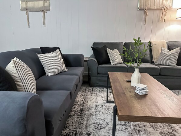 A modern living room with two grey sofas, striped pillows, a wooden coffee table, and a plant. - NEW! GR Modern & Updated 2BR Retreat - Sleeps 8, Near Downtown! (Grand Rapids)