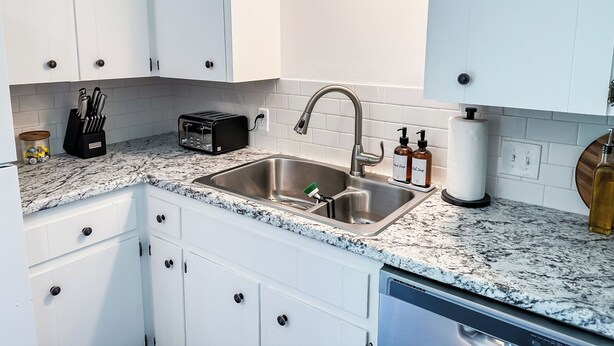 A modern kitchen with white cabinets, a stainless steel sink, a toaster, and a dish soap dispenser.