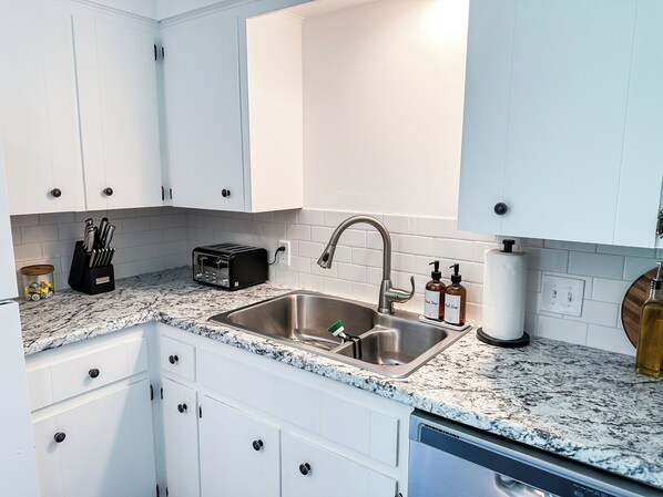 A modern kitchen with white cabinets, a stainless steel sink, a toaster, and a dish soap dispenser.