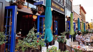 An outdoor seating area with tables and chairs, potted plants, and umbrellas at Butcher's Union.