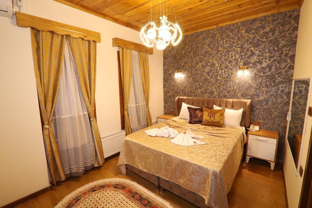 A hotel room with a bed, curtains, a nightstand, and a wall with a marble-like pattern.