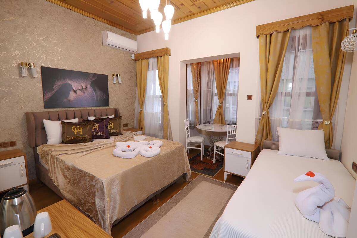 A hotel room with a bed, a desk, a chair, a table, a painting, and a window with curtains.