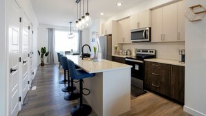 Een moderne keuken met een centraal eiland, barkrukken en roestvrijstalen apparatuur.
