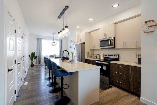 A modern kitchen with a central island, bar stools, and stainless steel appliances.