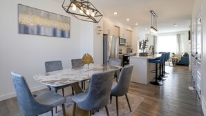 Een moderne keuken met een centraal eiland, roestvrijstalen apparatuur en een eethoek met een marmeren tafel en grijs gestoffeerde stoelen.