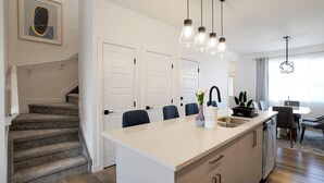 Een moderne keuken met een centraal eiland, een zithoek met tafel en stoelen, en een trap naar een hoger niveau.