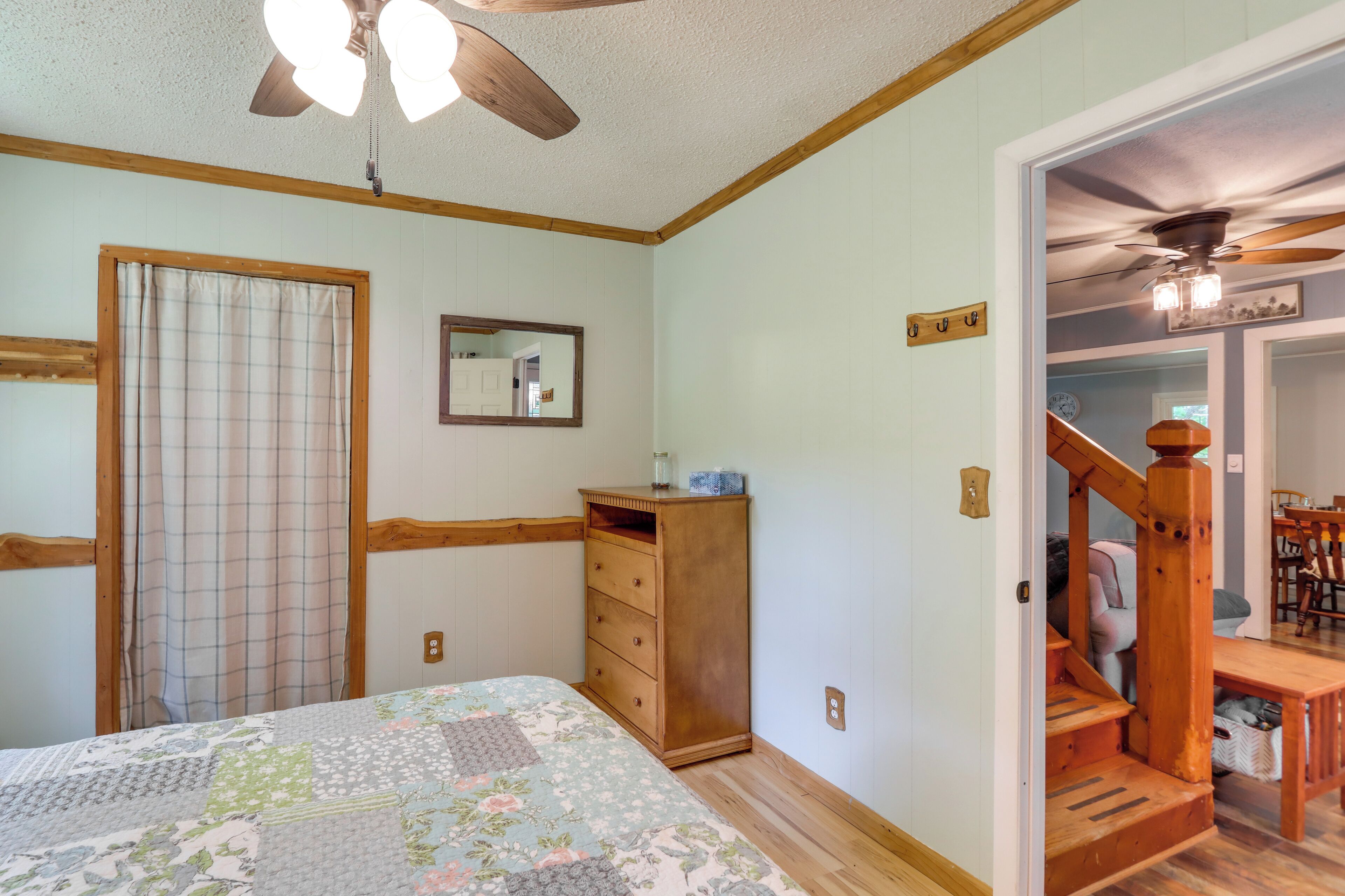 A bedroom with a bed, wooden dresser, and a staircase leading to another room.