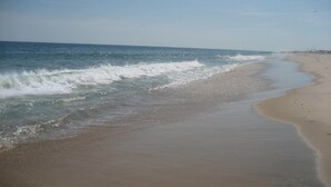 A beach with waves gently lapping at the shore, a clear sky, and a distant pier. - Steps to the beach!  Relax and Enjoy! (Amagansett)