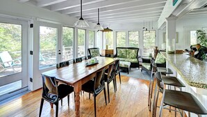 A spacious kitchen with a wooden table, bar stools, and a large window overlooking a deck. - Steps to the beach!  Relax and Enjoy! (Amagansett)