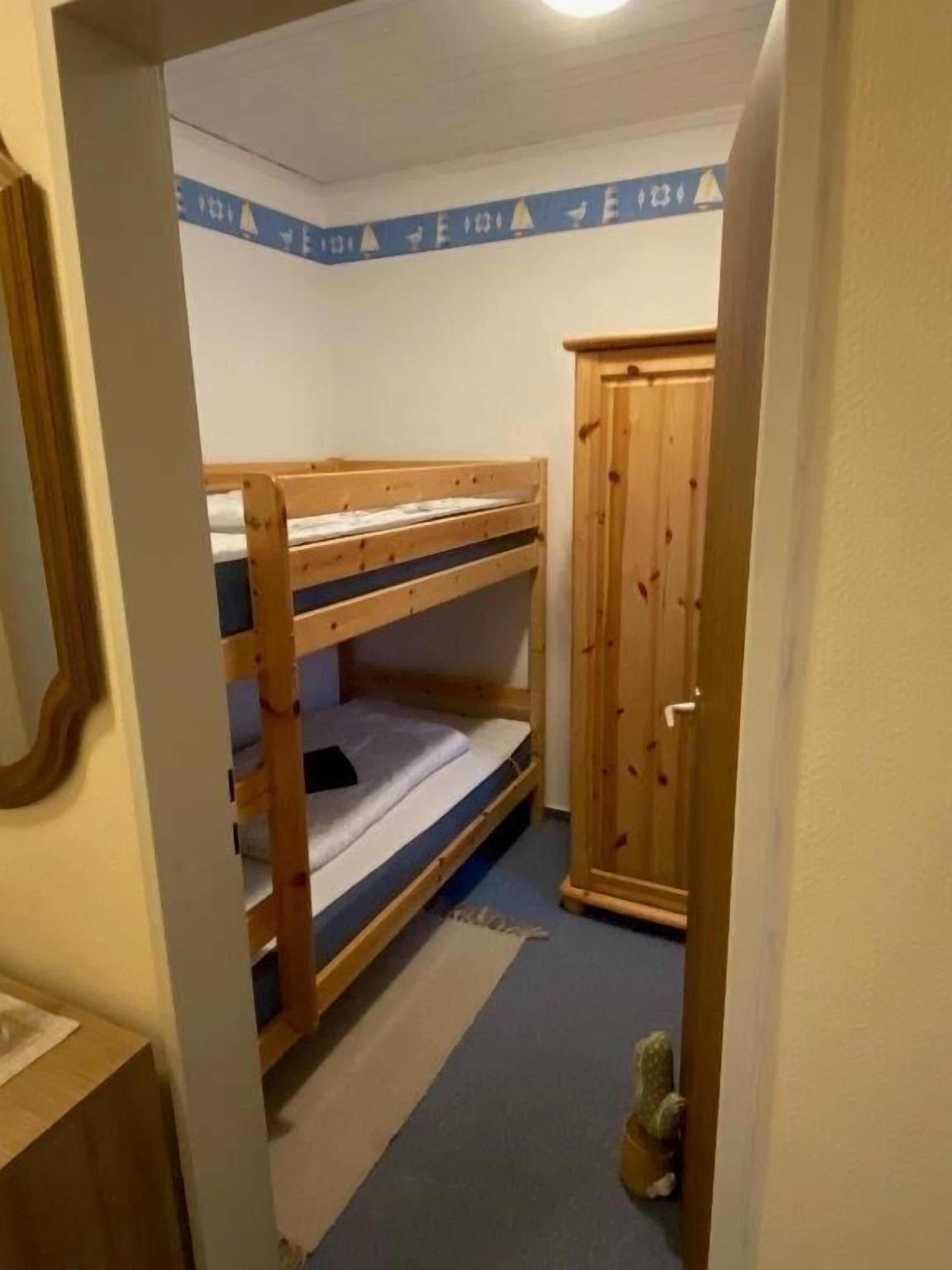 A bunk bed room with a wooden wardrobe and a small rug on the floor.