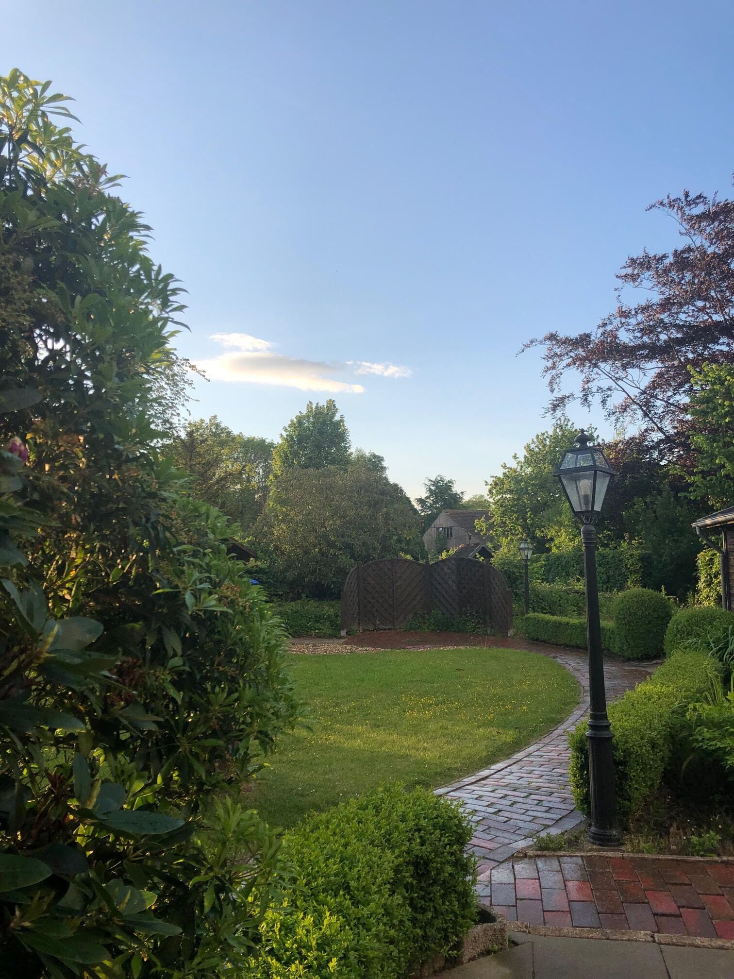 Un camí de jardí amb vora de maó, envoltat de vegetació exuberant i un cel clar.