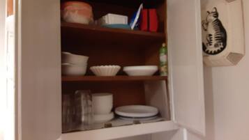 A kitchen cabinet with white dishes, a red container, and a bottle.