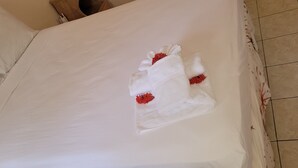 Ein ordentlich bezogenes Bett mit weißen Leinentüchern und einem dekorativen Handtuch mit roten Blumen.