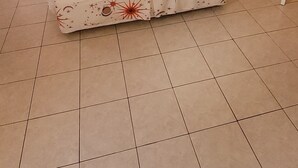 Ein ordentlich bezogenes Bett mit weißer Bettdecke, zwei Nachttische mit Lampen, ein Bild an der Wand und ein gefliester Boden.
