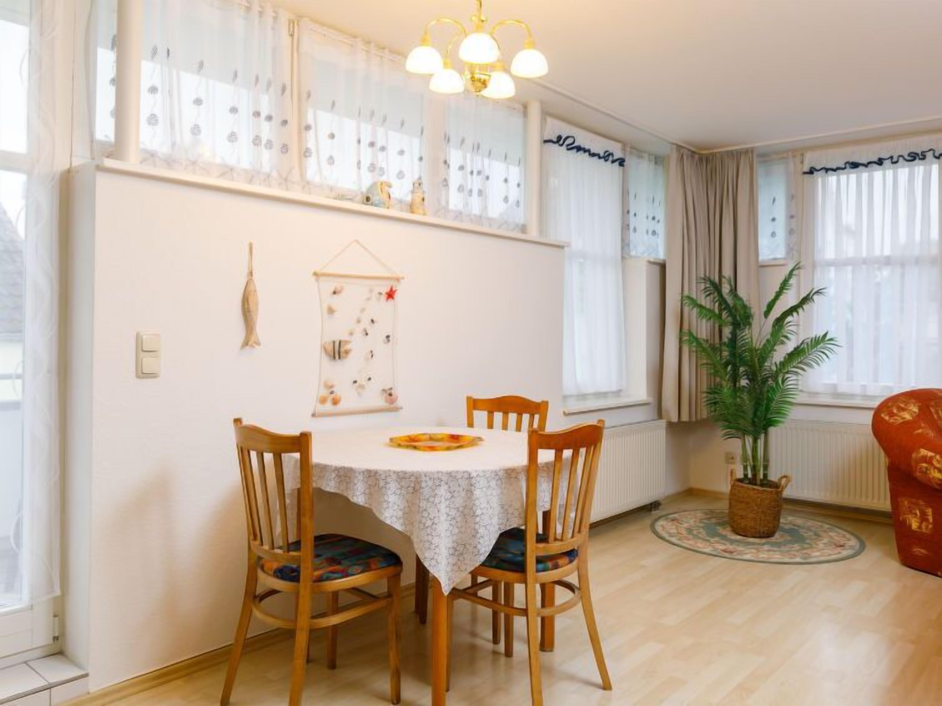 Un comedor con una mesa redonda, cuatro sillas de madera y una araña.