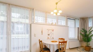 Un comedor con una mesa redonda, cuatro sillas de madera, una lámpara colgante y una planta en maceta.