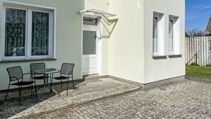 Un bâtiment à l’extérieur blanc, doté d’un patio couvert avec deux chaises et une table, ainsi que d’une petite fenêtre à cadre blanc.