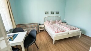 Une chambre à coucher comprenant un lit, un bureau, une chaise, une table de chevet et un berceau.
