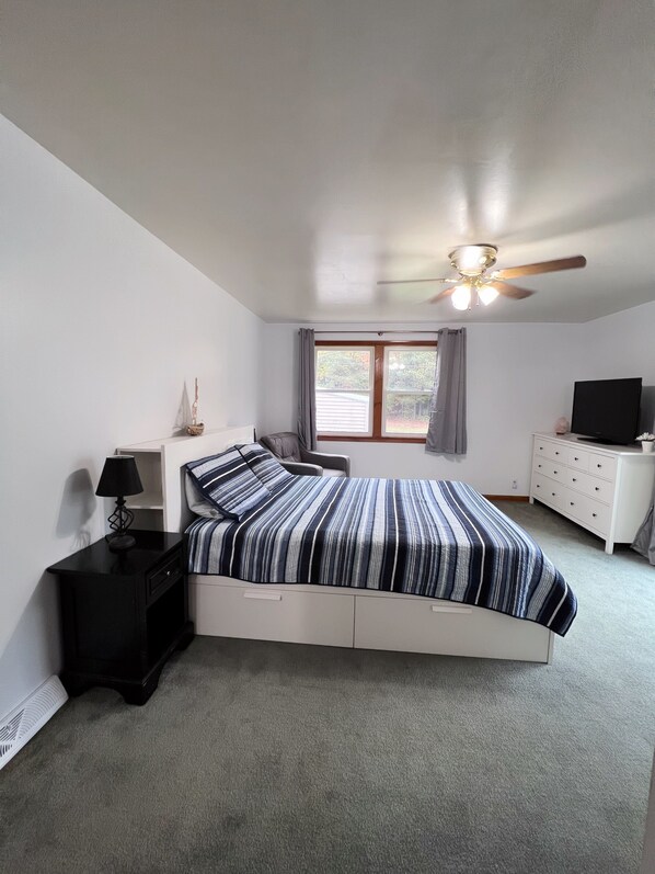 A bedroom with a bed, a nightstand, a dresser, a ceiling fan, and a window with curtains. - Hot tub, Nature, Parks and Beaches! Right in between Holland and Grand Haven. (West Olive)