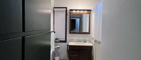A narrow hallway leading to a bathroom with a toilet, sink, and mirror.
