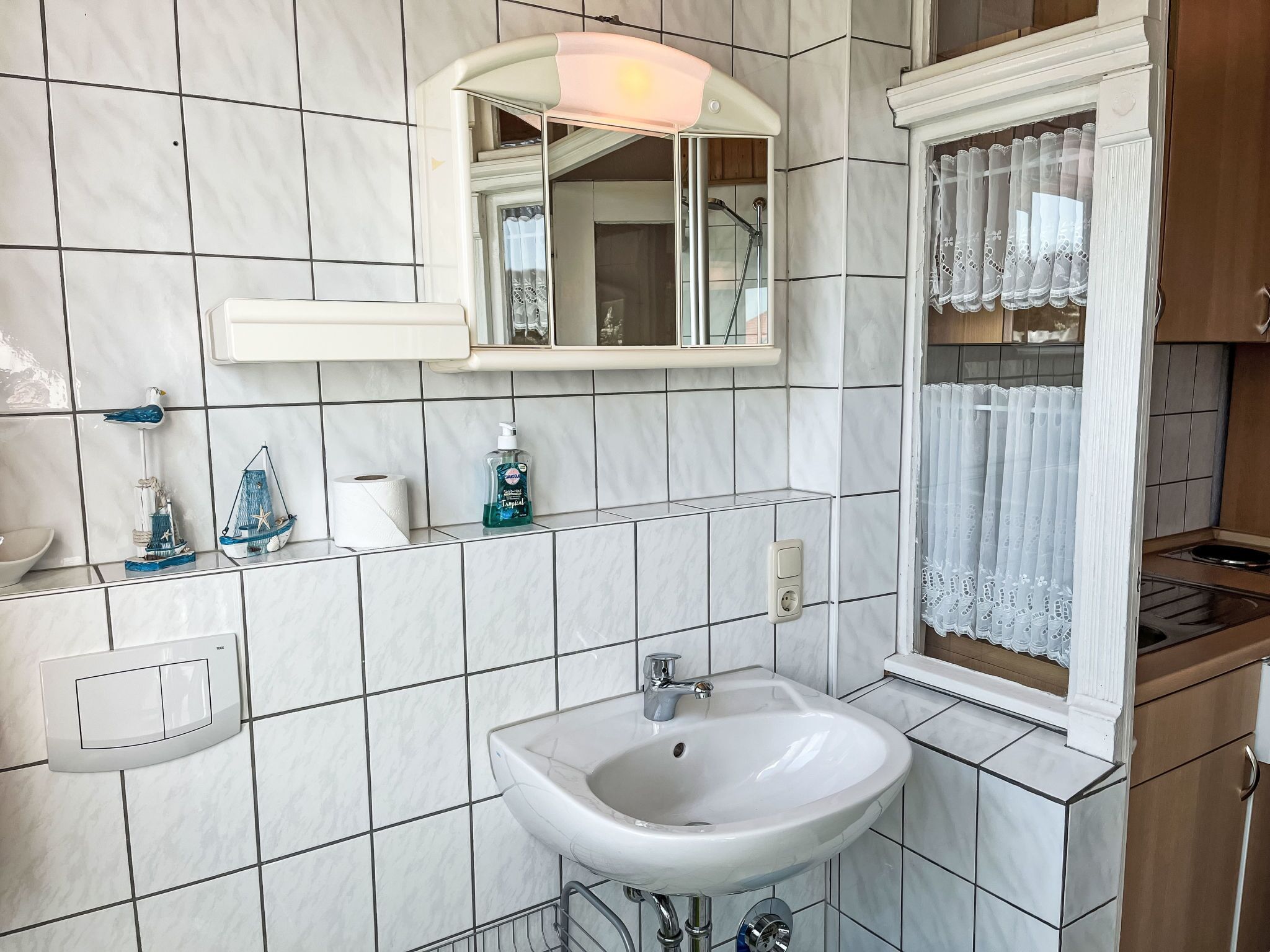 A bathroom with a white sink, a mirror, and a window with lace curtains.