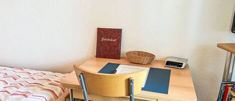 Une petite pièce comprenant un lit, un bureau avec une chaise, un panier, une radio Sony et une bibliothèque.