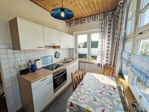 A compact kitchen with white cabinets, a black stove, and a window with curtains.