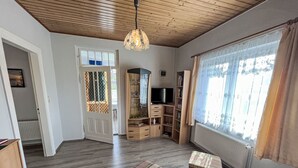 Een ruime woonkamer met houten vloeren, een televisie, een boekenkast en een raam met gordijnen.