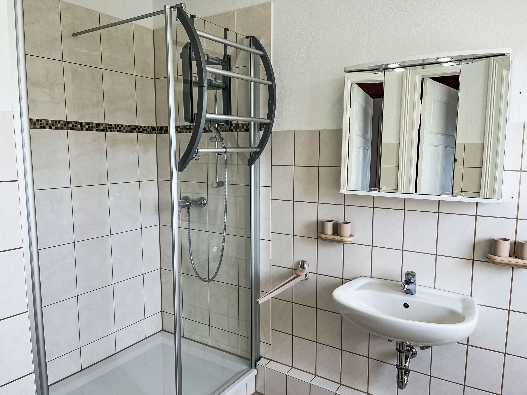 A bathroom with a glass shower enclosure, a white sink, and a mirror above it.