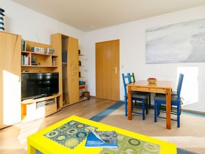 Un espace de vie compact comprenant un meuble TV en bois, une table à manger avec des chaises et une bibliothèque.