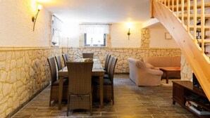 A cozy living room with a stone wall, a wooden staircase, a dining table with wicker chairs, and a sofa. - Vacation home Petra by Interhome (Neeberg)