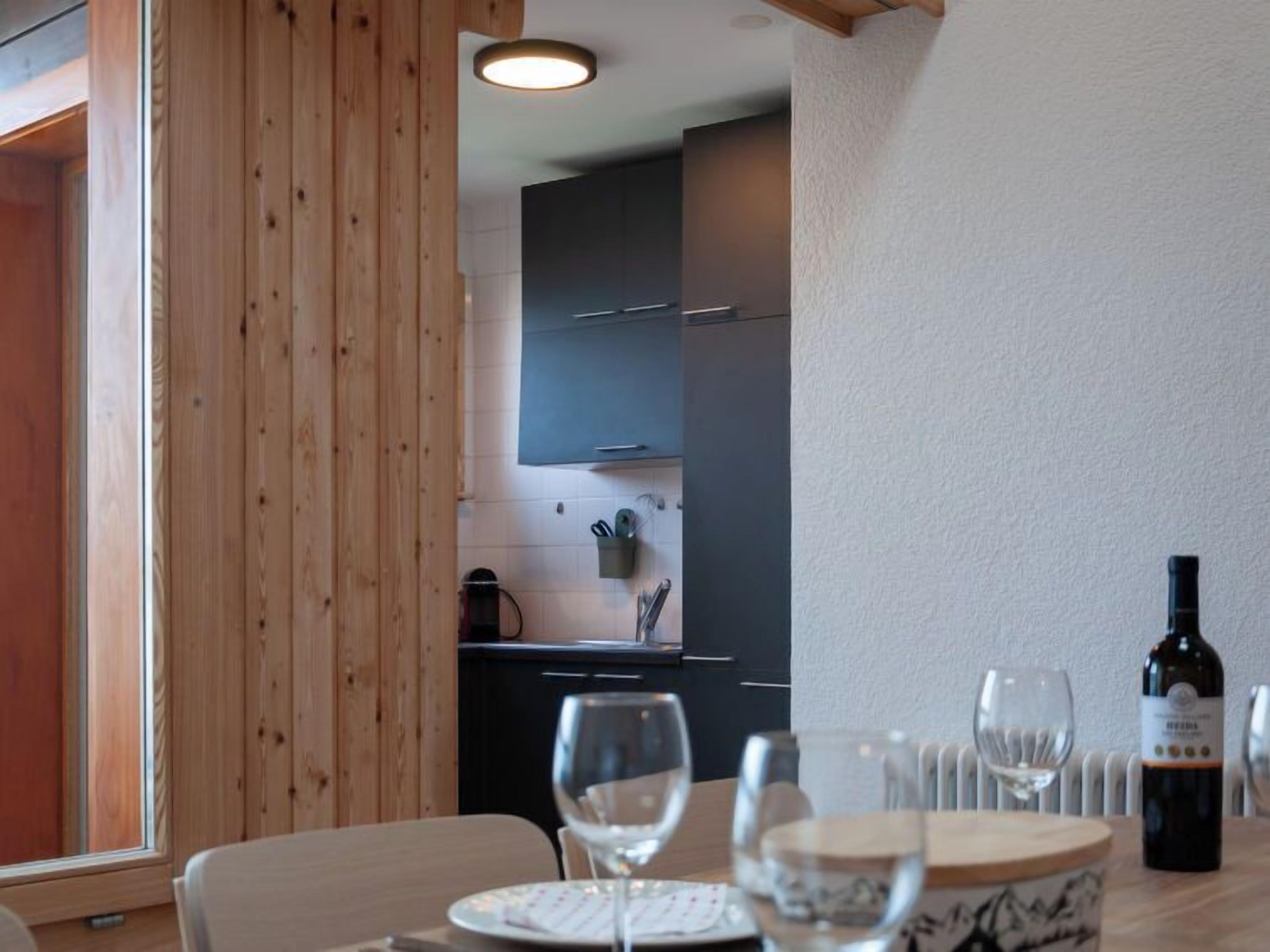 Un comedor con una mesa dispuesta para dos, una botella de vino y una ventana con persianas de madera.