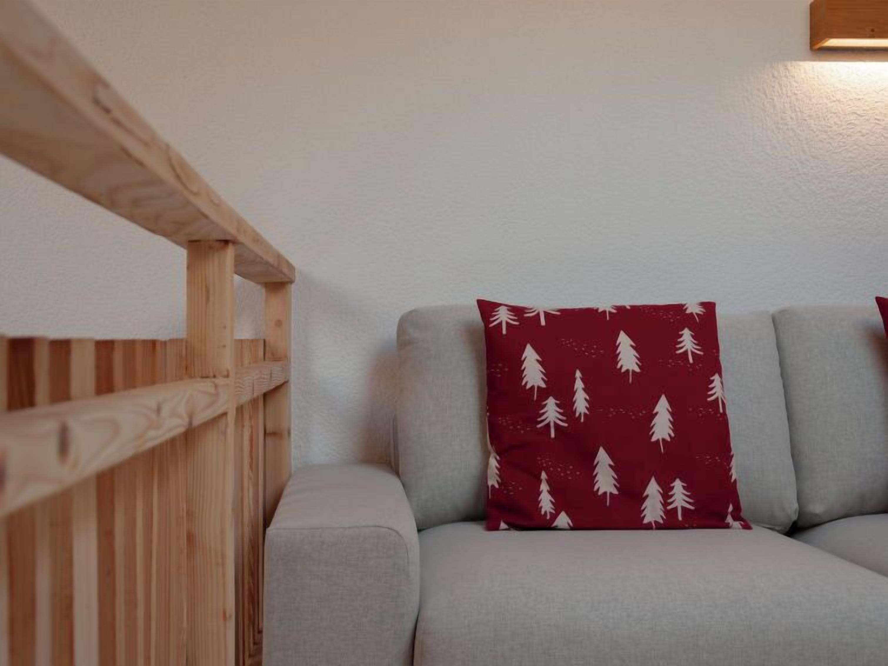 A room with a wooden bunk bed, a grey sofa, and a red pillow with a tree pattern.