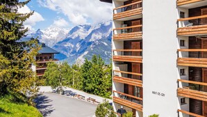 A modern building with wooden balconies, a clear view of snow-capped mountains, and a parking area with benches. - Haut de Cry 16 by Interhome (Nendaz)