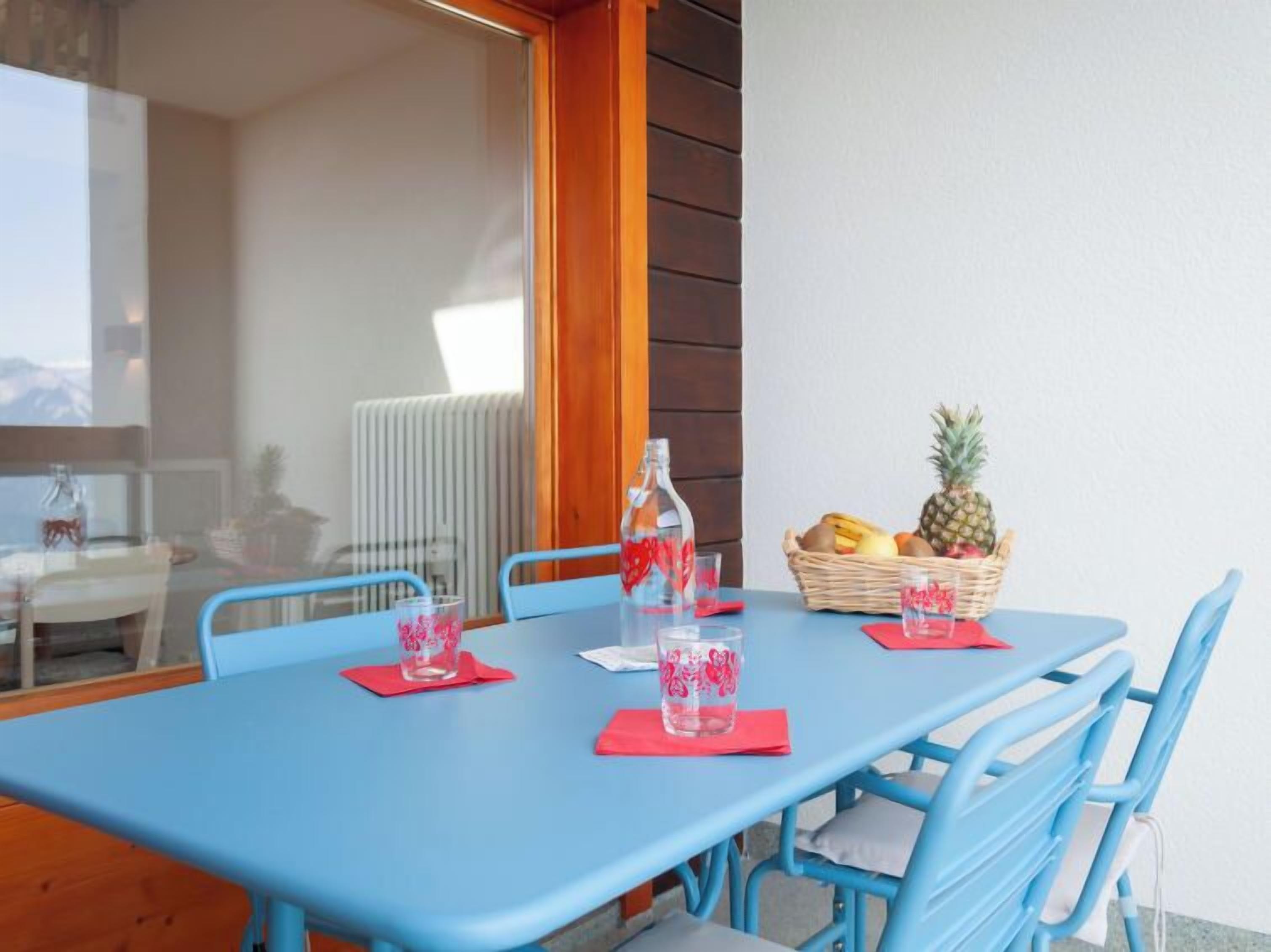 A blue table with four chairs, a bottle of water, and a basket of fruit on the table.