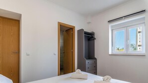Un dormitorio con puerta de madera, armario, cama con toallas, cómoda y ventana con vistas.