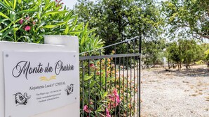 Letrero de 'Monte da Churra' con información de contacto y vista de un jardín con una reja de metal.