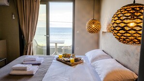 Habitación de hotel con cama, bandeja de desayuno, vista al mar y lámpara colgante.