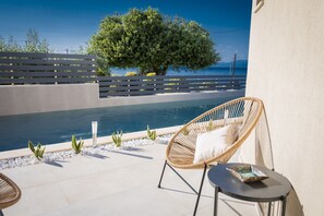A poolside area with a wicker chair, a small table, and a view of the sea. - Theros Suites (Sikyona)
