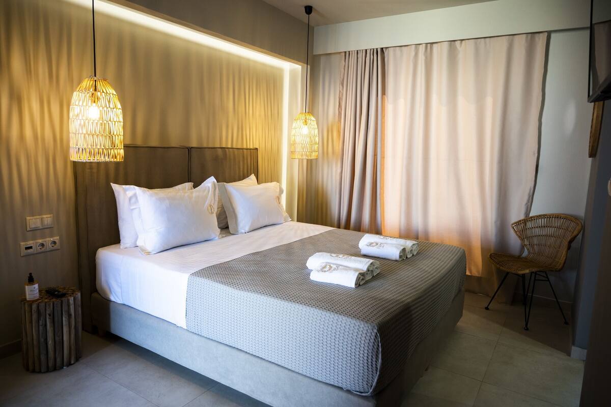 Habitación de hotel con una cama grande, dos lámparas de noche, una silla y un taburete pequeño.