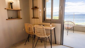 Una habitación con una mesa, dos sillas de mimbre, un ventanal con vista al mar y estantes empotrados con objetos decorativos.
