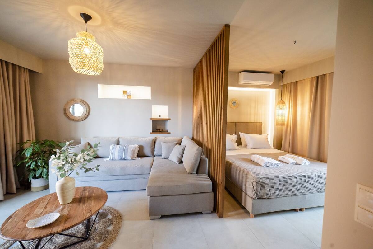 Una habitación de hotel moderna con un sofá, una cama, una mesa de centro de madera y una lámpara colgante.